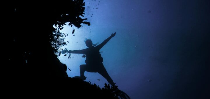 Silhouette of scuba diver exploring coral reef in deep blue ocean